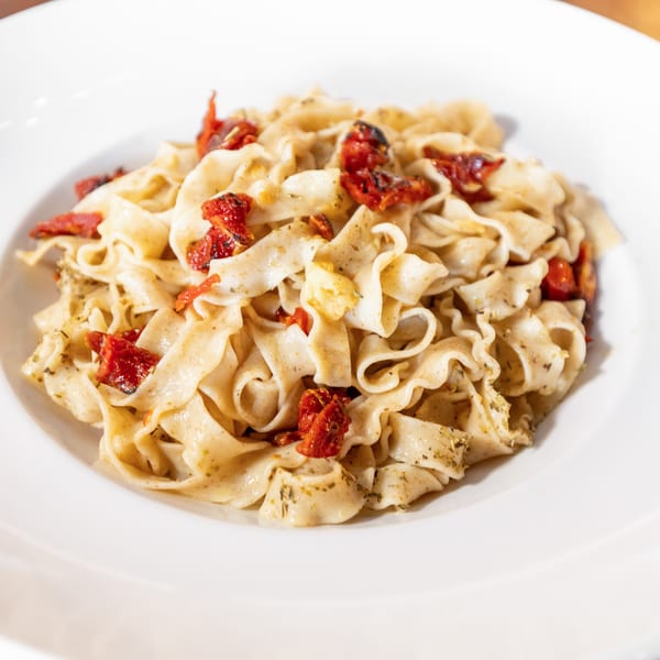 Close-up of pasta with sun-dried tomatoes and herbs in a white bowl.