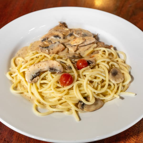 Creamy mushroom spaghetti with cherry tomatoes on a white plate, viewed from above.