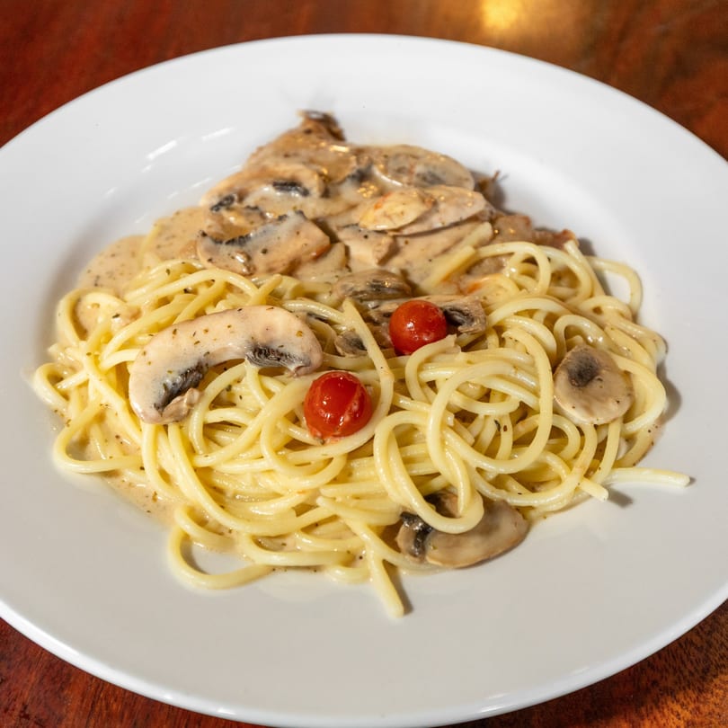 Creamy mushroom spaghetti with cherry tomatoes on a white plate, viewed from above.