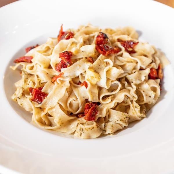 Close-up of pasta with sun-dried tomatoes and herbs in a white bowl.