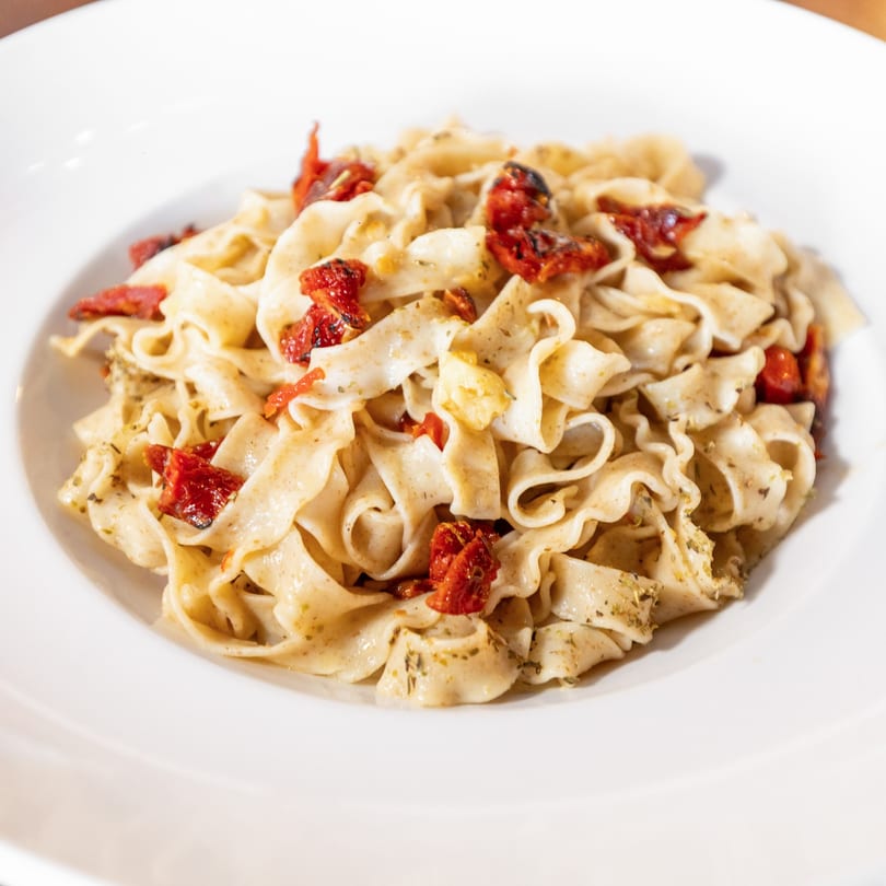 Close-up of pasta with sun-dried tomatoes and herbs in a white bowl.
