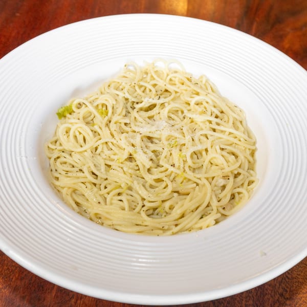 Close-up of spaghetti with pesto sauce and grated cheese in a white bowl on a wooden table.