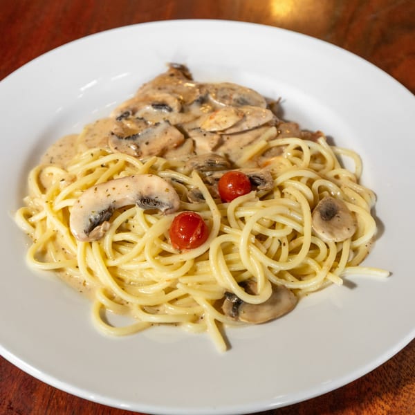Spaghetti with creamy mushroom sauce and cherry tomatoes on a white plate.