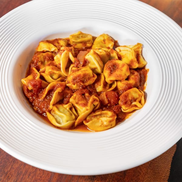 Tortellini pasta in a rich red tomato sauce, served in a white bowl on a wooden table.