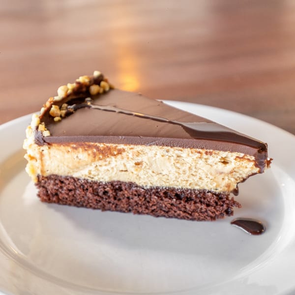 A slice of chocolate cake with a peanut butter layer, topped with chocolate ganache and nuts.