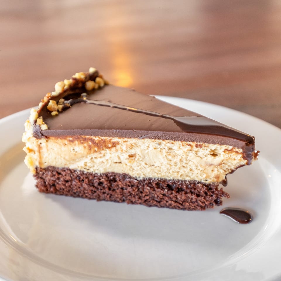 A slice of chocolate cake with a peanut butter layer, topped with chocolate ganache and nuts.