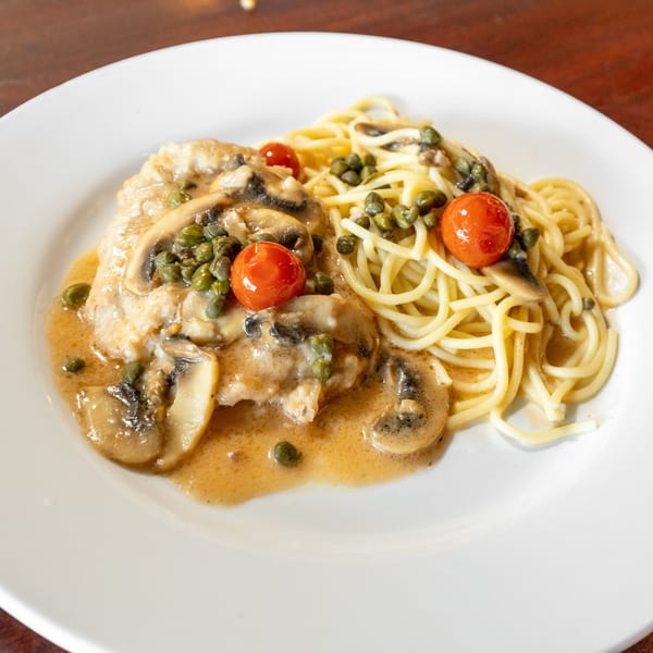 Chicken piccata with mushrooms, capers, cherry tomatoes, and spaghetti on a white plate.