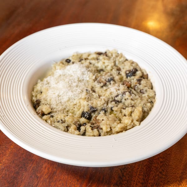 Creamy mushroom risotto topped with grated Parmesan cheese in a white bowl on a wooden table.