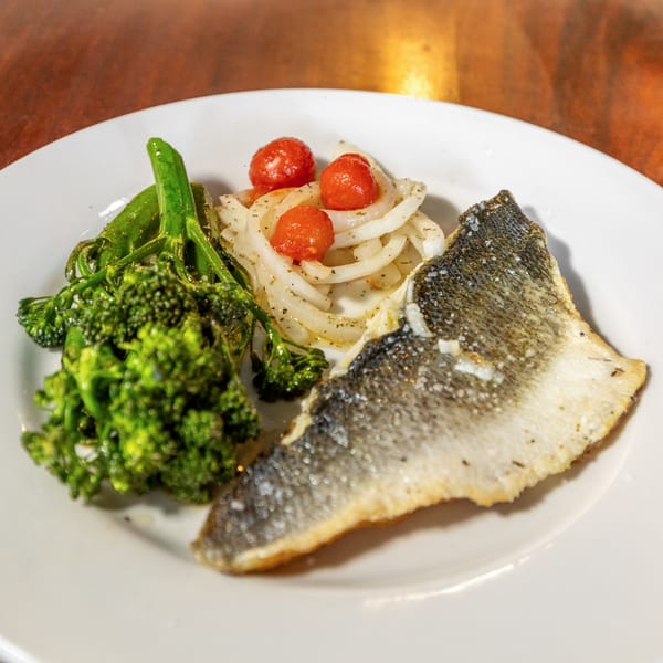 Pan-seared fish with crispy skin, broccolini, and a side of pickled onions and cherry tomatoes.