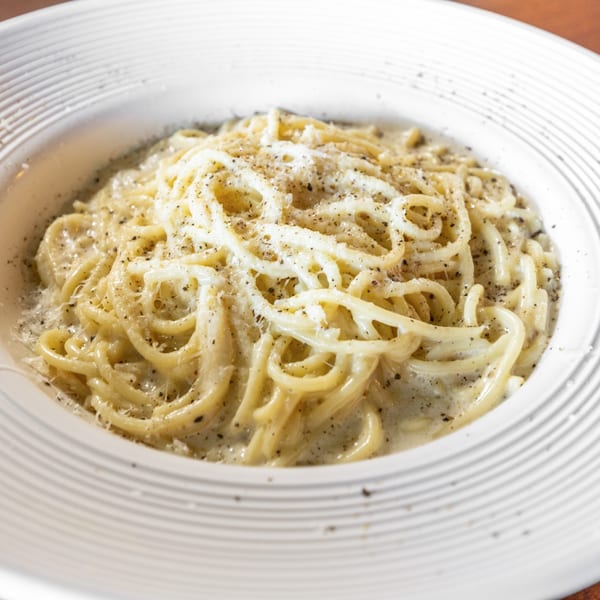 Creamy spaghetti carbonara with generous black pepper and grated cheese in a white bowl.