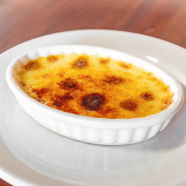Close-up of a crème brûlée in a white oval ramekin on a white plate.