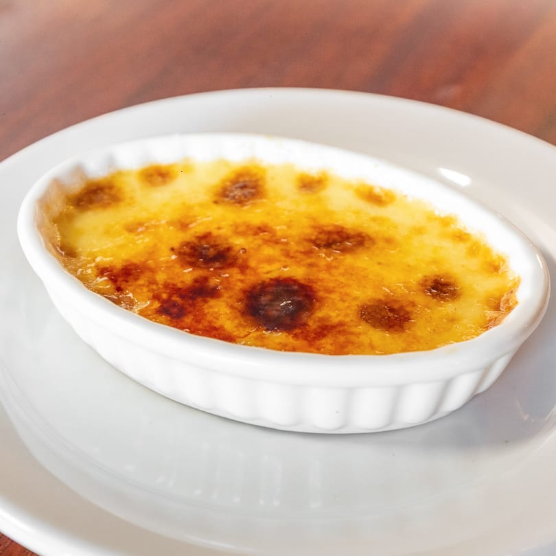 Close-up of a crème brûlée in a white oval ramekin on a white plate.