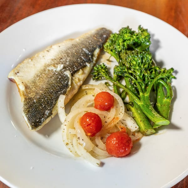 Pan-seared fish fillet with crispy skin, broccolini, and a side of cherry tomatoes and onions.