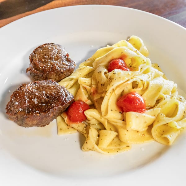 Two seared beef medallions with salt flakes next to pasta with cherry tomatoes and herbs.